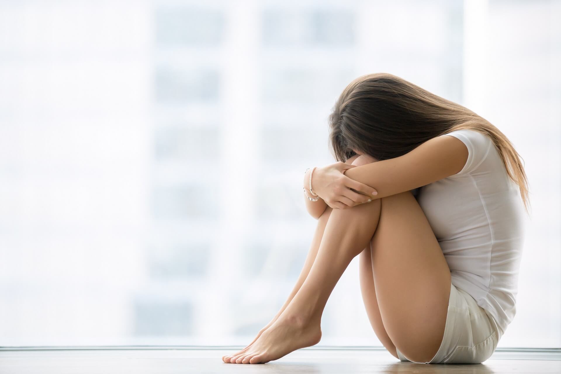 young-woman-sitting-near-the-window-her-head-down-PFEYVNC